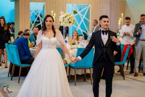 Newlyweds hold hands while dancing at reception with blue decor and white floral arrangements.