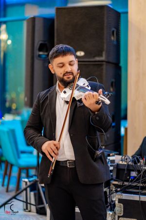Musician in formal attire performing with a microphone in a venue with turquoise ambient lighting.