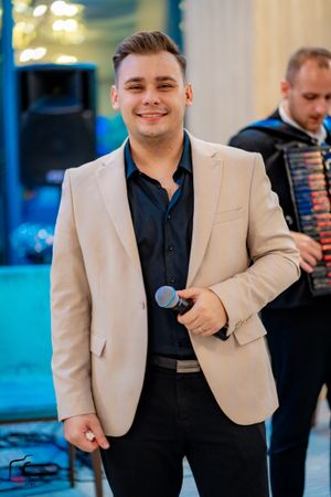 Entertainer in beige jacket and dark shirt performing at an indoor venue with decorative lighting.