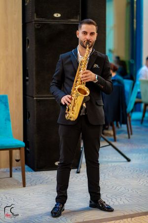 Performer playing saxophone in black suit during indoor entertainment event.