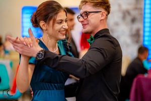 Elegant dance partners smiling while moving across a beautifully lit ballroom floor.