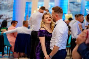 Wedding guests dancing together at a reception with blue lighting and stone wall backdrop.