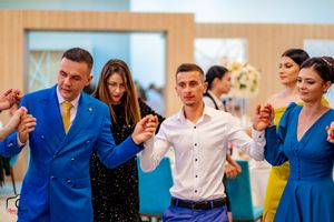 Wedding guests in bright blue attire dance together in a line formation at an indoor celebration.