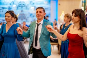 Celebration attendees in colorful formal wear perform coordinated dance moves at an indoor venue.