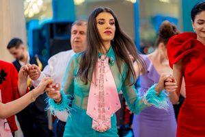 Dancer in turquoise outfit with pink scarf moves expressively at a formal gathering.
