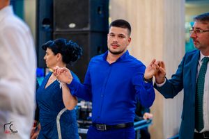 Dancers in formal attire hold hands during group dance at indoor event.