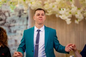 Wedding guests in suits and dresses dance together at an elegant reception with white floral arrangements.