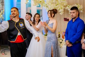 Wedding party and guests dancing in formal attire at a decorated indoor reception venue.