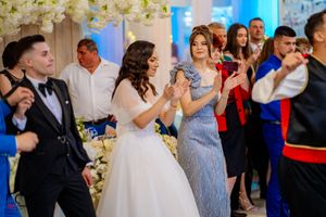 Celebration at a wedding venue with guests dancing under floral decorations and blue lighting.