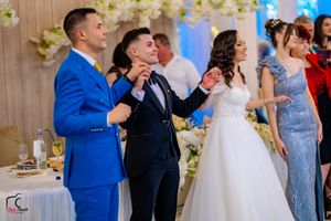 Wedding party dancing and celebrating in a banquet hall with white floral arrangements.