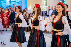 Women in traditional folk costumes with red headpieces performing a cultural dance.