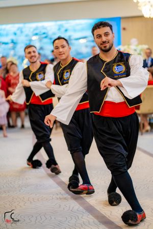 Traditional dancers in black and white costumes performing choreographed moves on a patterned floor.
