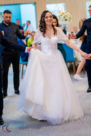 Bride in flowing white gown dances joyfully at wedding reception.