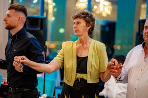 Dancers hold hands in a line during a social dance event with turquoise walls and warm lighting.