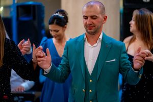 Dancer in teal blazer holding hands during traditional line dance at indoor venue.