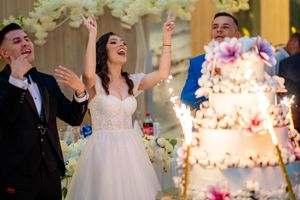 Wedding celebration with guests celebrating joyfully next to an elegant tiered cake with sparklers.