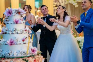 Wedding party celebrates enthusiastically around a beautifully decorated tiered cake at reception.