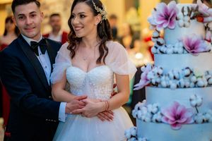 Elegant wedding reception featuring couple posing beside their ornate tiered cake with purple flowers.