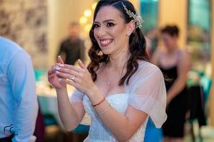 Wedding reception guest in white dress clapping and smiling during celebration.