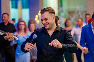 An entertainer in black attire performs with a microphone at an event with colorful lighting.