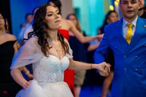 A bride in a white beaded gown dances energetically at a wedding reception.