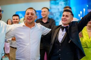 Guests in formal attire celebrate enthusiastically at an event with blue lighting.