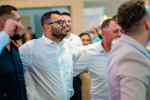 Group of party guests in white shirts and formal wear dancing together at an indoor event.