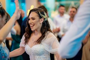 A bride in a white dress dances joyfully at a wedding reception with blue lighting in the background.