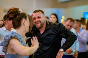 Wedding guests laughing and dancing together during a lively reception celebration.
