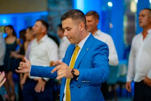 Man in bright blue suit and yellow tie dances energetically at wedding reception.