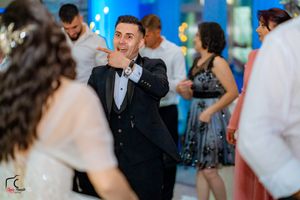 Guest in formal black tuxedo makes animated gesture while dancing at reception.