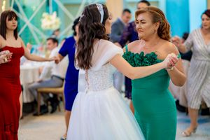Guests in colorful formal attire dance together at a wedding reception with blue ambient lighting.