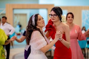 Wedding guests in colorful dresses dance together during reception festivities.