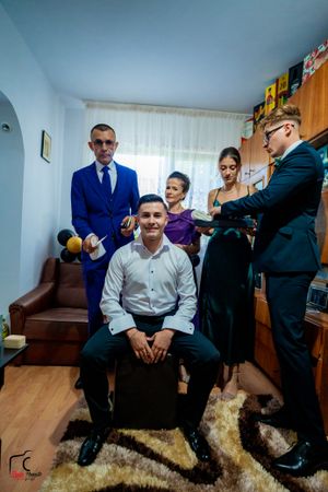 A group gathers in a small room with wooden furniture and a bright blue suit stands out among formal attire.