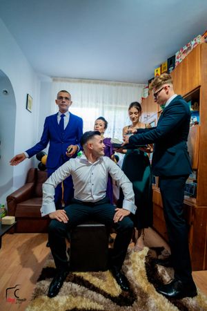 People in formal attire interact animatedly in a living room setting with wooden flooring.