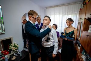 Wedding party members gather in a bright room as formal attire adjustments are made before the ceremony.