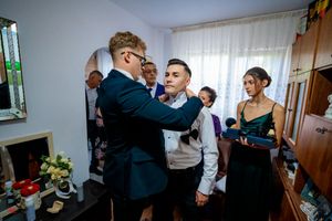 A formal bow tie adjustment takes place during pre-wedding preparations while attendants watch nearby.