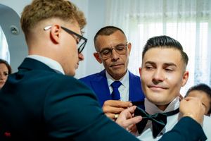 Careful adjustment of a bow tie during pre-wedding preparations while others watch attentively.
