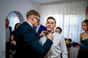 Pre-wedding scene showing the meticulous adjustment of formal wear in a bright indoor setting.