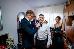 Wedding party members gather as formal attire is adjusted in a sunlit room before the ceremony.