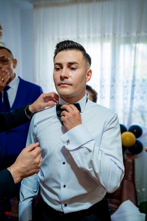 Wedding preparation scene showing the adjustment of a formal bowtie against a white shirt.