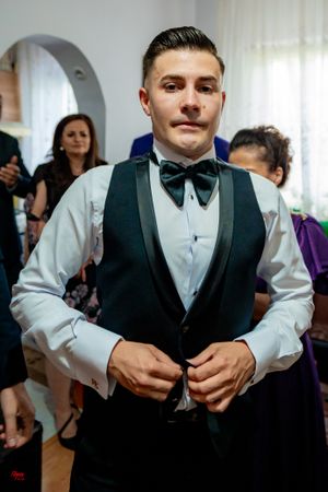 Person in white shirt and black vest smiles during formal event preparations.