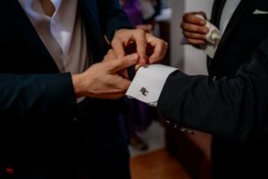 Close-up of hands adjusting formal attire cufflinks during wedding preparation.
