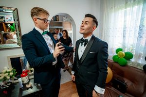 Men in tuxedos preparing for formal event with green balloons in background.