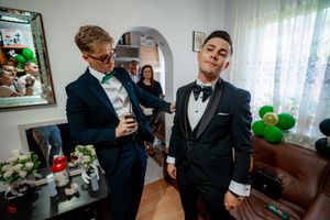 Wedding party members helping each other dress in decorated living room setting.