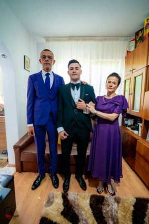Family portrait in formal wear with a bright blue suit, dark tuxedo, and purple dress against white curtains.