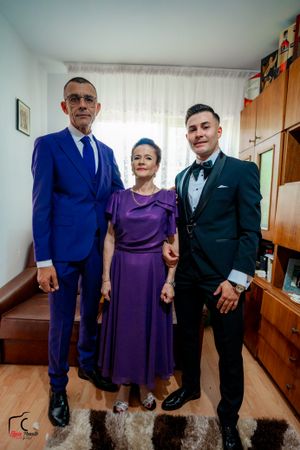 Three people pose in formal attire with bright blue suit and purple dress in a home setting.