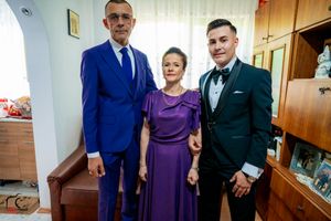 Three people in formal attire pose together in a living room with an arched doorway.