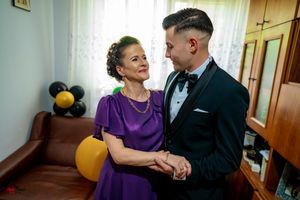 A couple dances intimately in formal attire against a light-filled interior setting.