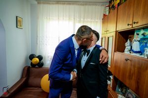People in formal attire share a dance in an interior space with yellow balloons visible.